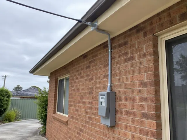 Overhead service cable and bracket on a brick house exterior with meter box in Hamlyn Terrace