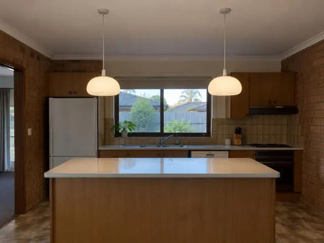 Kitchen with two pendant lights over an island, tiled walls and window above the sink in Warnervale
